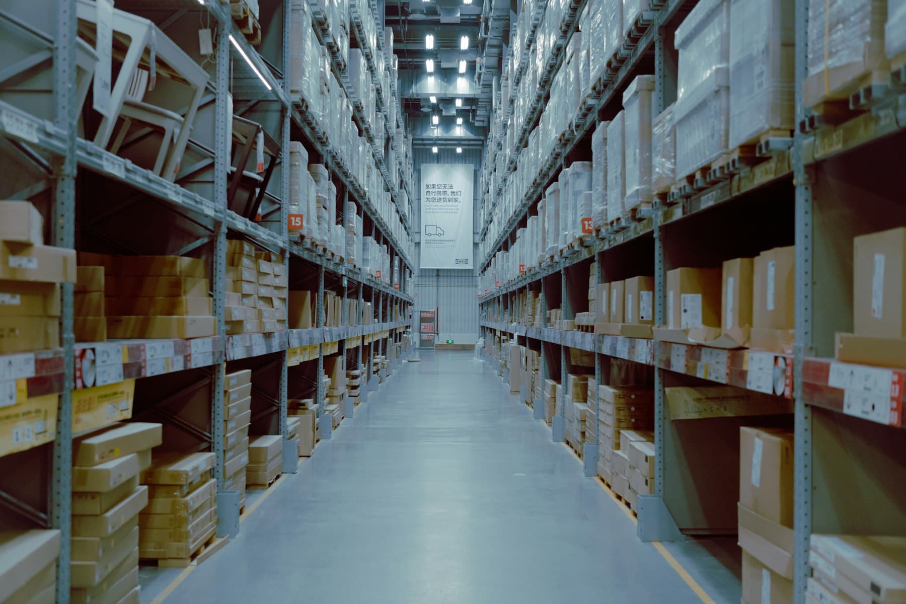 A long, orderly warehouse aisle between tall shelving stacked with boxes.