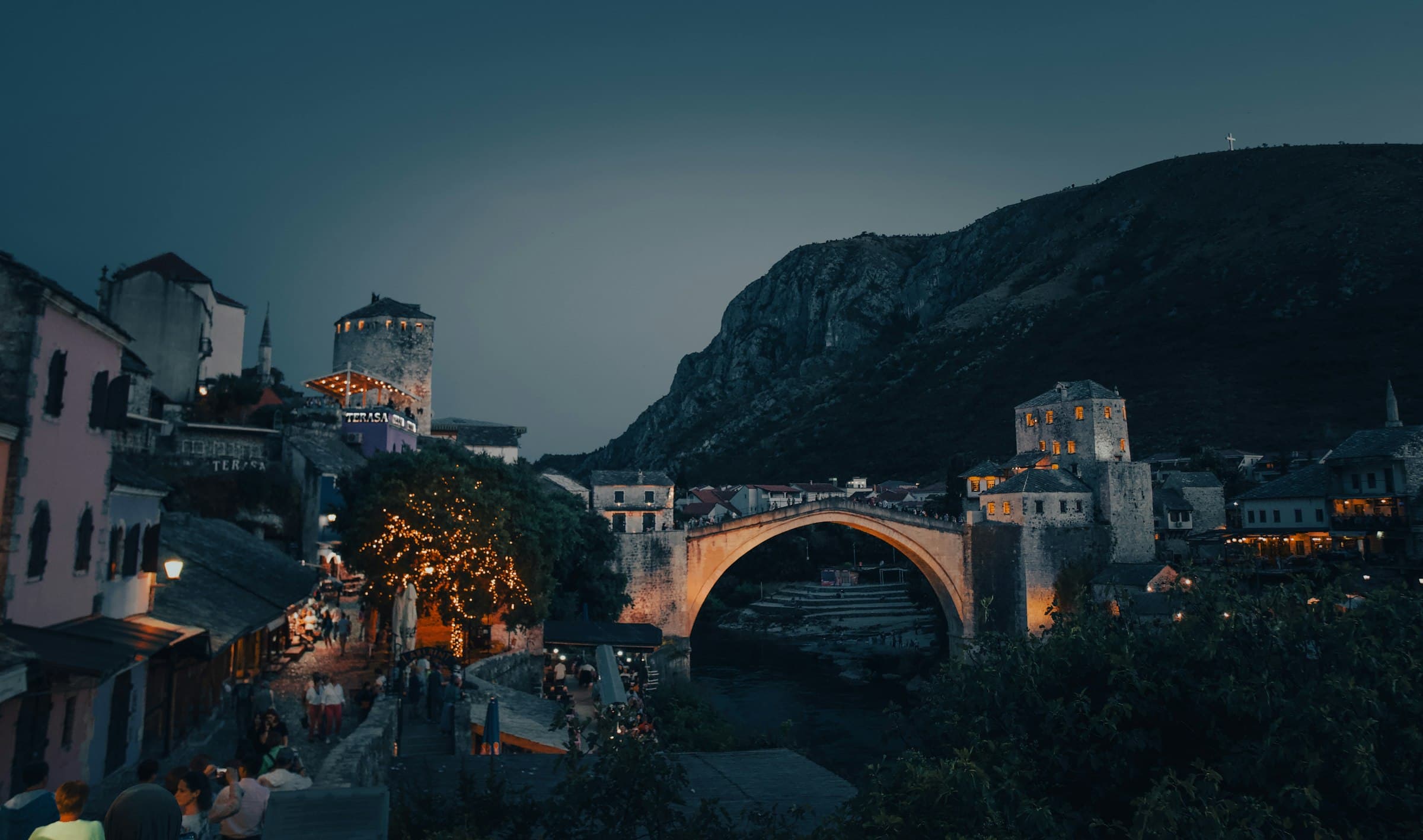 The Old Bridge in Mostar at dusk, with the old town lit beneath the mountains.